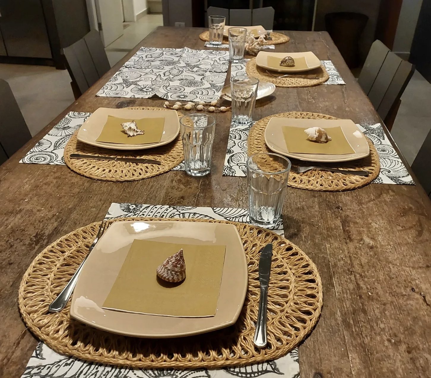 Mesa de madeira com quatro lugares, sousplats de palha e conchas